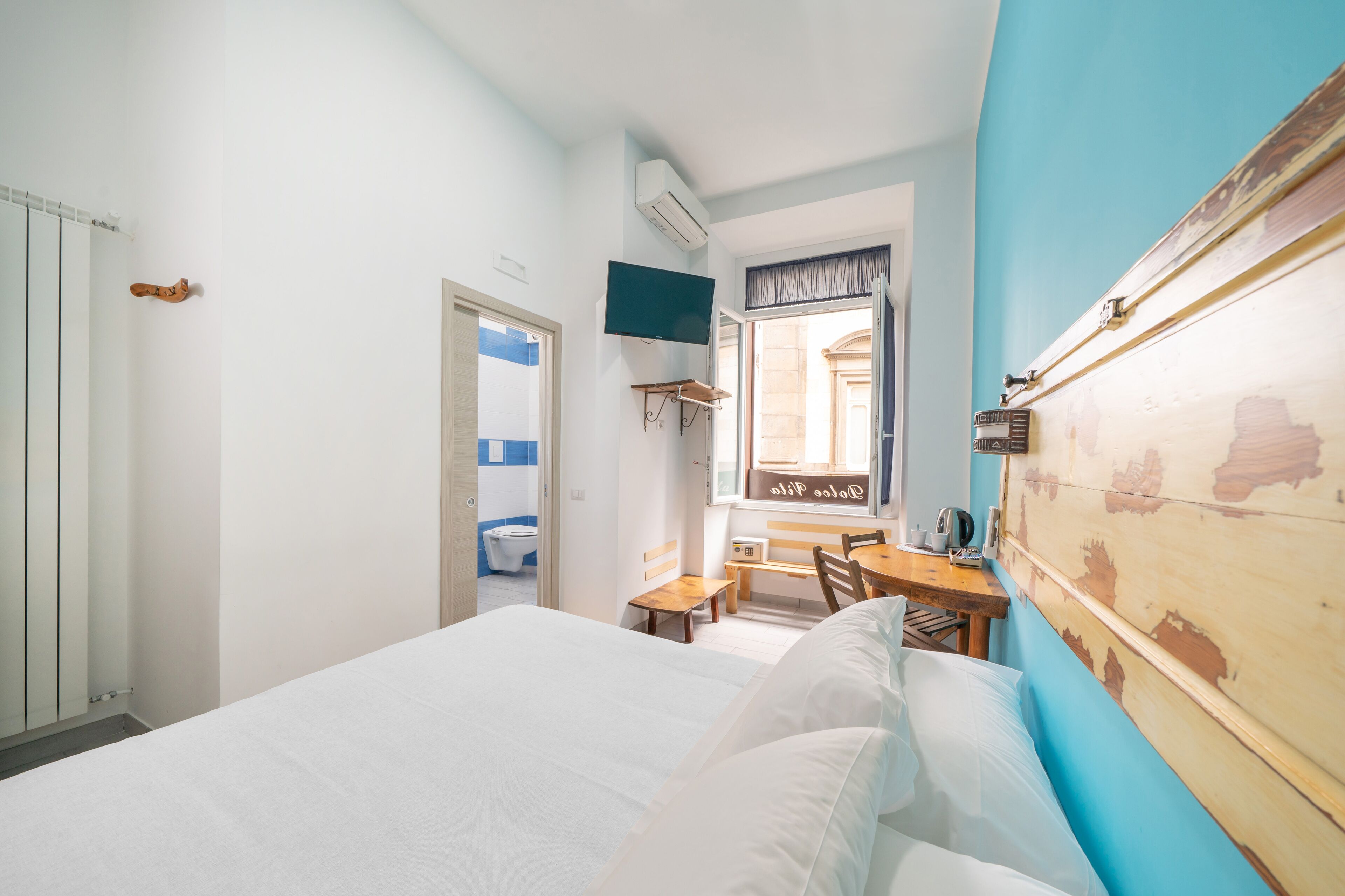 A hotel room with a bed, a desk, a chair, a television, and a bathroom visible through an open door.