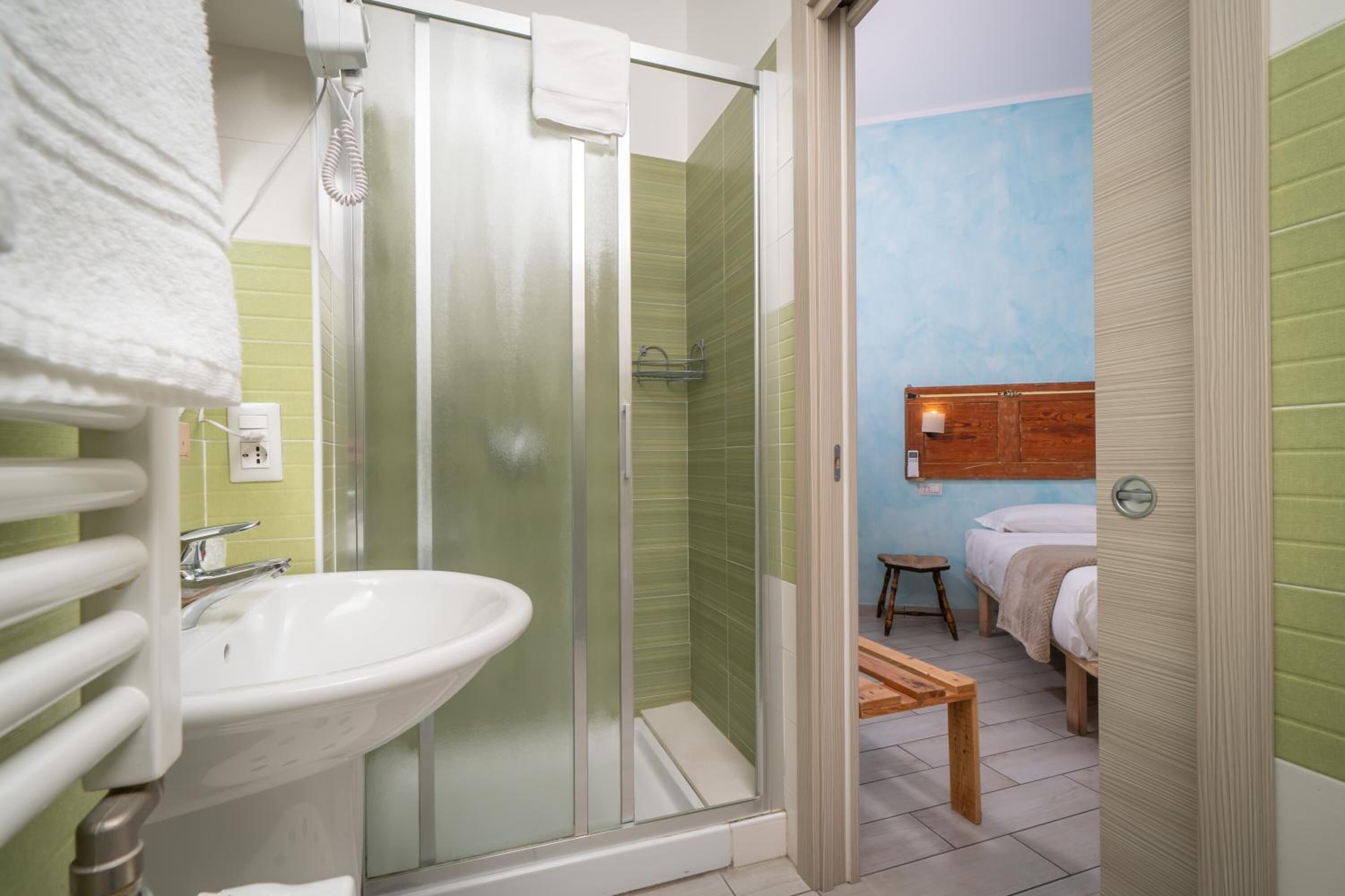 Un baño con ducha de vidrio, lavamanos blanco y banco de madera.