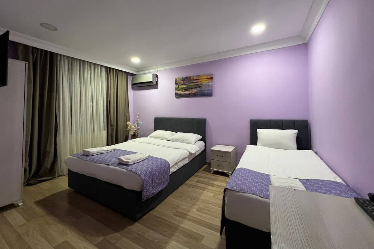 Habitación de hotel con dos camas, una mesita de noche pequeña, un televisor montado en la pared y una ventana con cortinas.