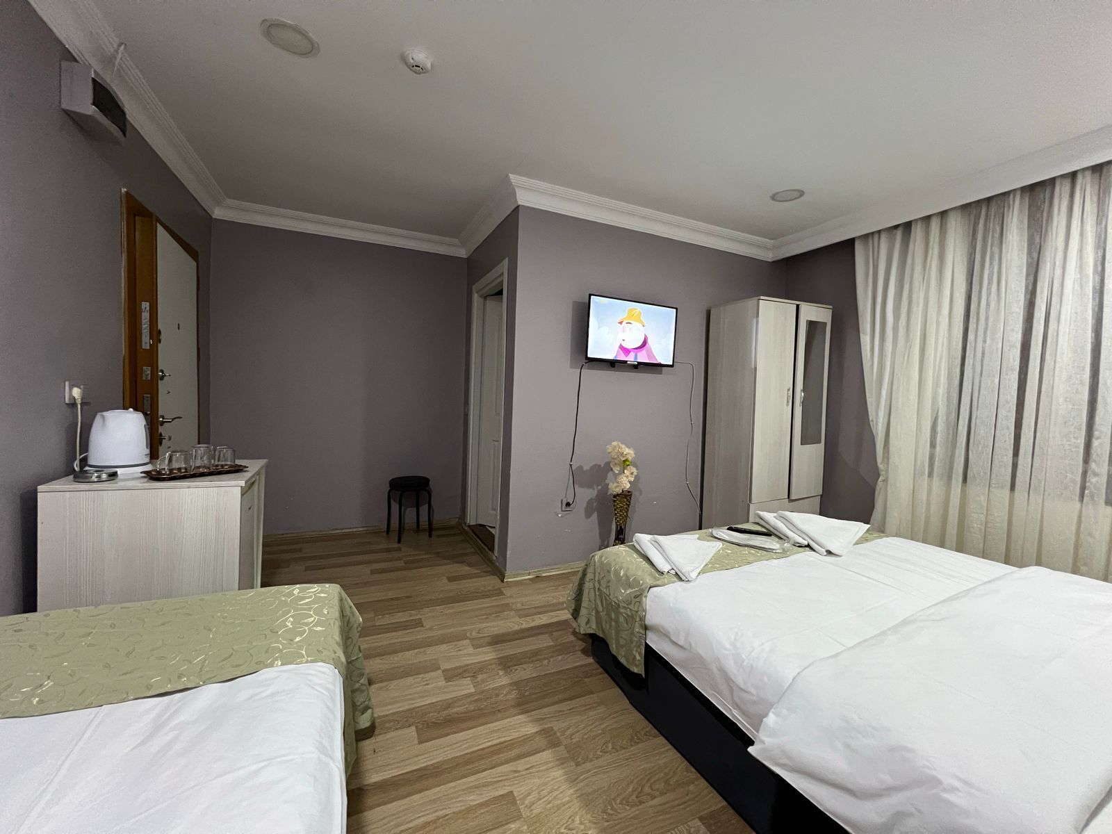 Une chambre d’hôtel avec deux lits, une télévision, une armoire et un bureau équipé d’une bouilloire et de verres.