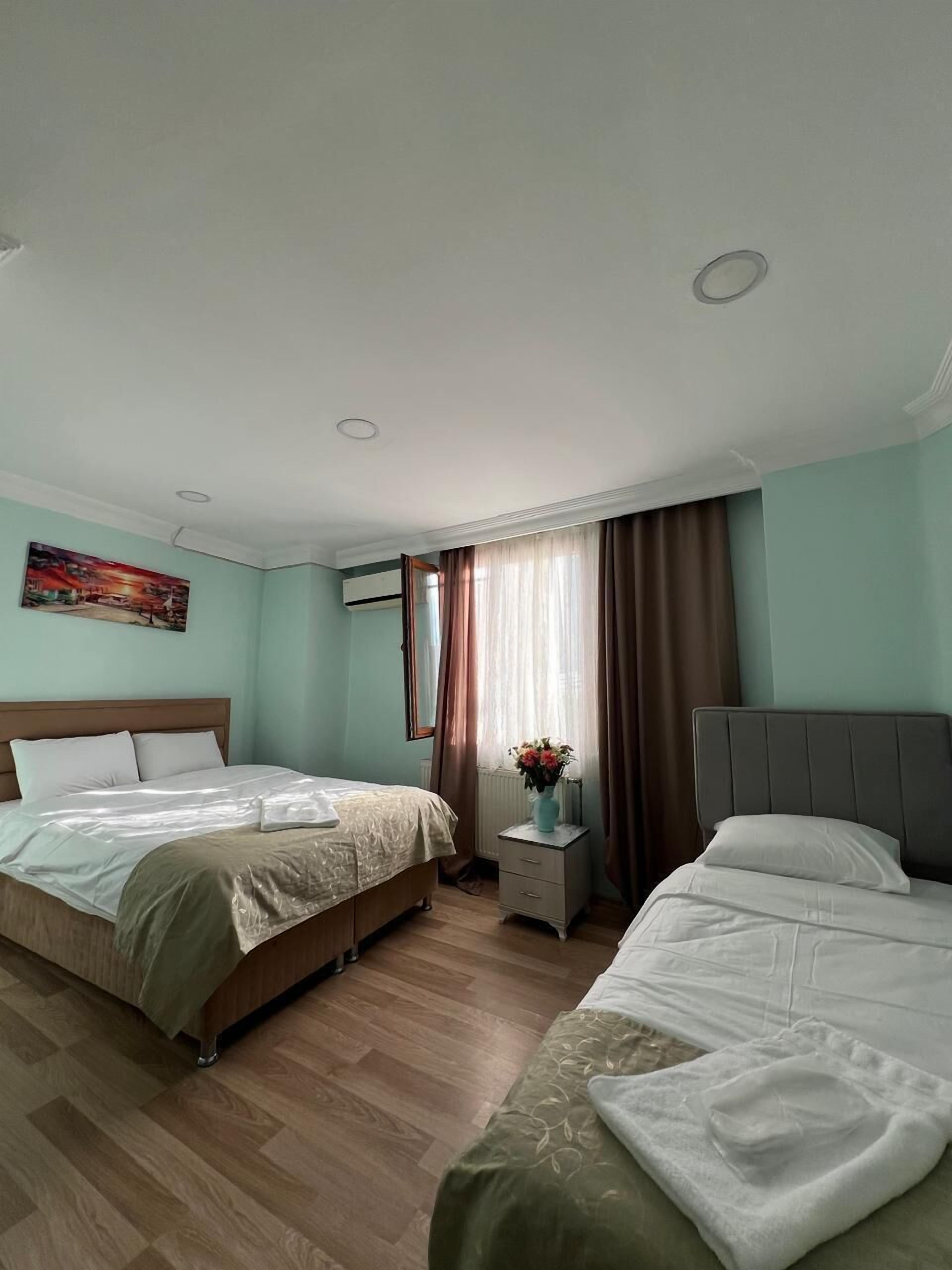 A hotel room with two beds, a nightstand with a vase of flowers, a painting on the wall, and a window with curtains.