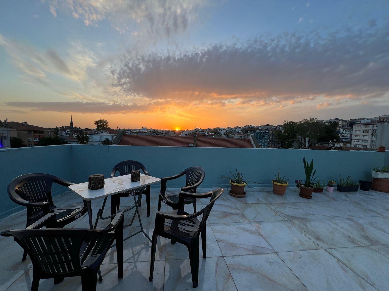 Une terrasse sur le toit, avec une table et des chaises, des plantes en pot et une vue imprenable sur le paysage urbain au coucher du soleil.