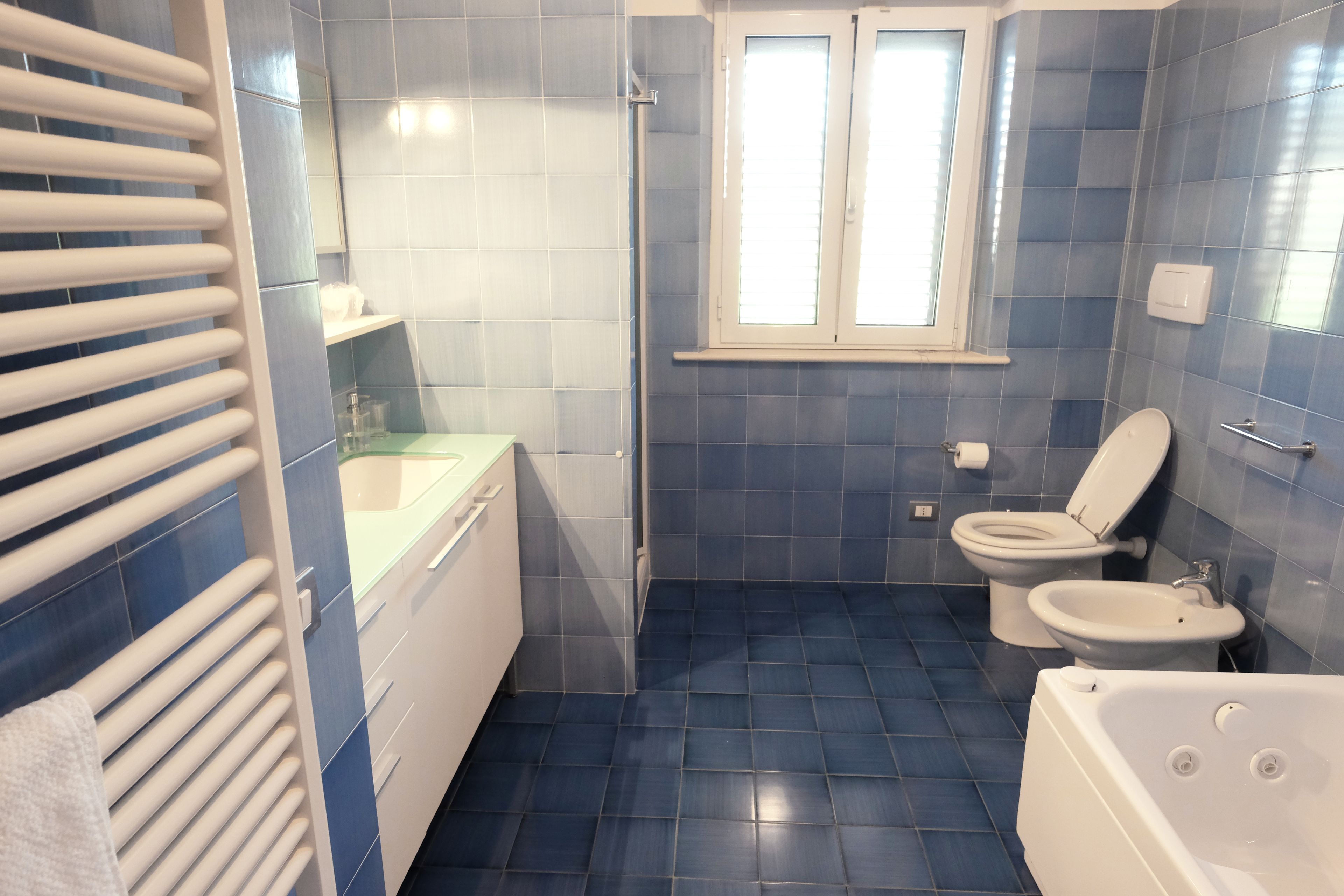 A bathroom with a bathtub, two toilets, a sink, and a window.