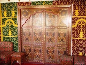 A room with a large ornate wooden door, patterned walls, and traditional cushions. - Hotel Zelis (Asilah)