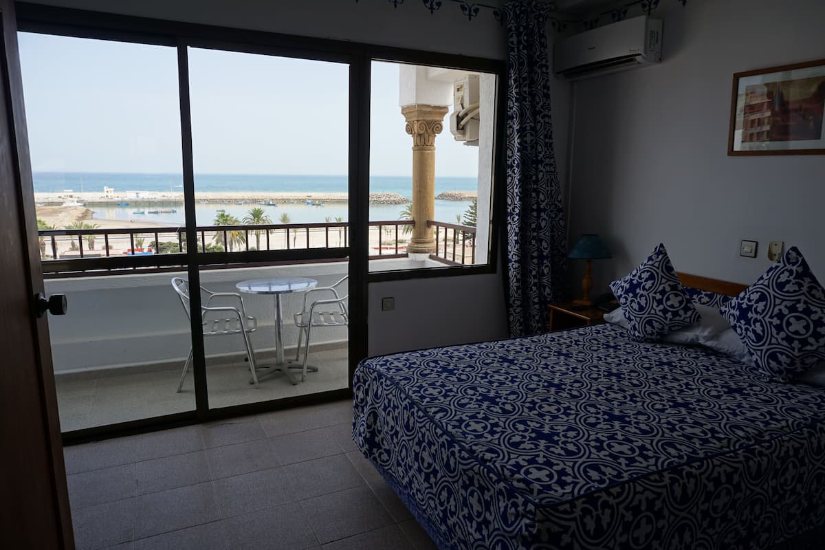 Una habitación con cama, un balcón con mesa y sillas, y vista al mar.