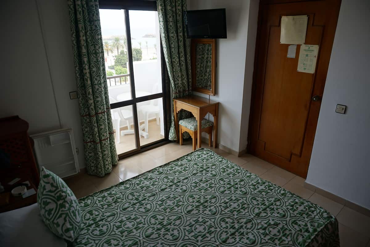 Una habitación de hotel con una cama, una pequeña mesa de madera con una silla, un televisor montado en la pared y una puerta con un aviso.