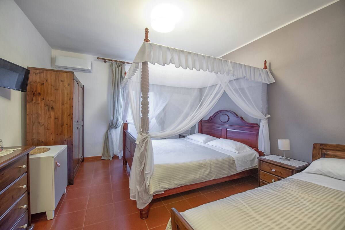 Ein Schlafzimmer mit Himmelbett, Holzschrank, Nachttisch mit Lampe und kleiner Schreibtisch mit Schubladen.