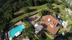 Vue aérienne d’un quartier résidentiel avec une piscine, une maison à toit de tuiles et de la végétation luxuriante tout autour.
