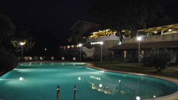 Une piscine illuminée la nuit, avec les bâtiments environnants et les lampadaires.