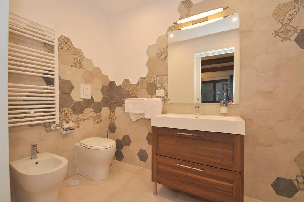 A modern bathroom with a hexagonal tile backsplash, a wooden vanity, a bidet, and a toilet.