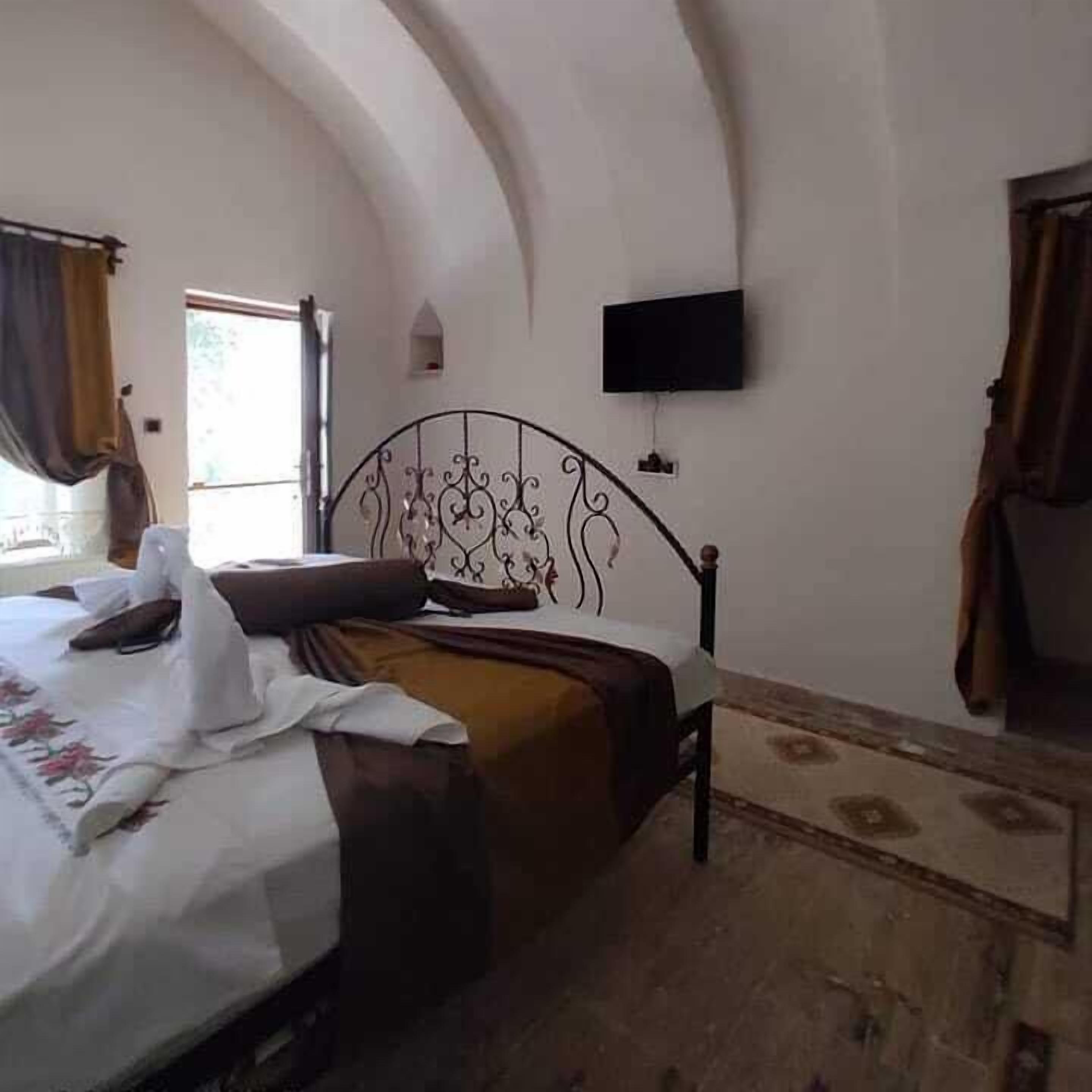 Une chambre à coucher avec un lit, un téléviseur fixé au mur et une fenêtre avec des rideaux.