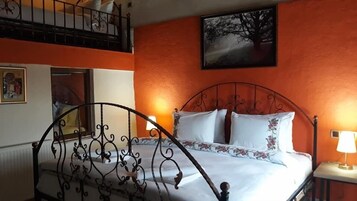 A double bed with ornate metal headboard, a nightstand with a lamp, and a painting on the wall.