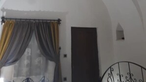 Una habitación con techo abovedado, una cama con cabecera oscura y una ventana con cortinas.