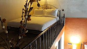 Un dormitorio con cama, ropa de cama blanca, baranda de metal y una escalera que lleva a otra habitación.