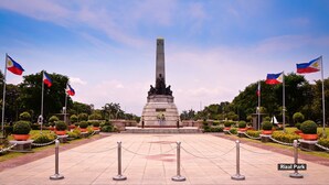 Un monumento con un obelisco alto, rodeado de plantas en macetas y banderas.