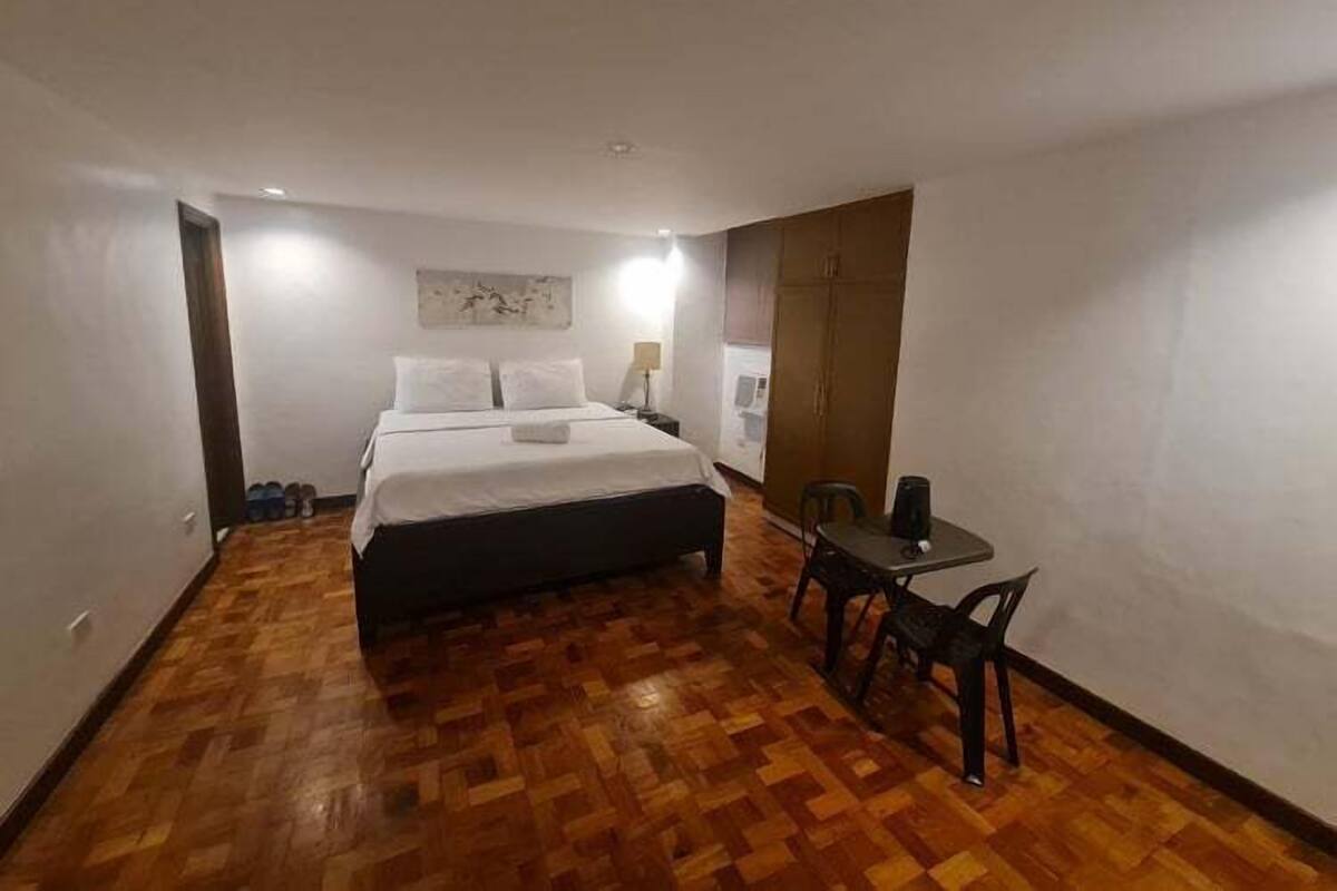 A hotel room with a bed, a small table with chairs, a lamp, and a wardrobe.