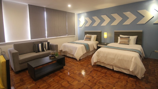 Una habitación de hotel con dos camas, un sofá, una mesita de centro y un ventanal con cortinas.