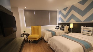 Habitación de hotel con dos camas, un sillón amarillo, una mesita con una planta y un televisor montado en la pared.