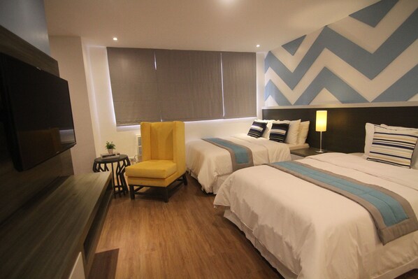 A hotel room with two beds, a yellow armchair, a small table with a plant, and a TV mounted on the wall. - Bryan Condo Makati (Makati)