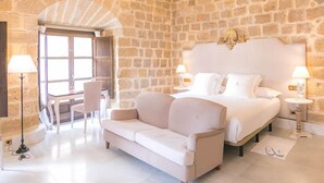 Quarto com parede de pedra, lustre, cama, sofá e área de jantar.