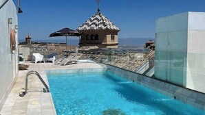 Uma piscina com água azul cristalina, um pequeno edifício com telhado telhado e um céu limpo.