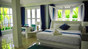 Una camera d'albergo moderna con un letto grande, una scrivania e vista su vegetazione lussureggiante dalle finestre.
