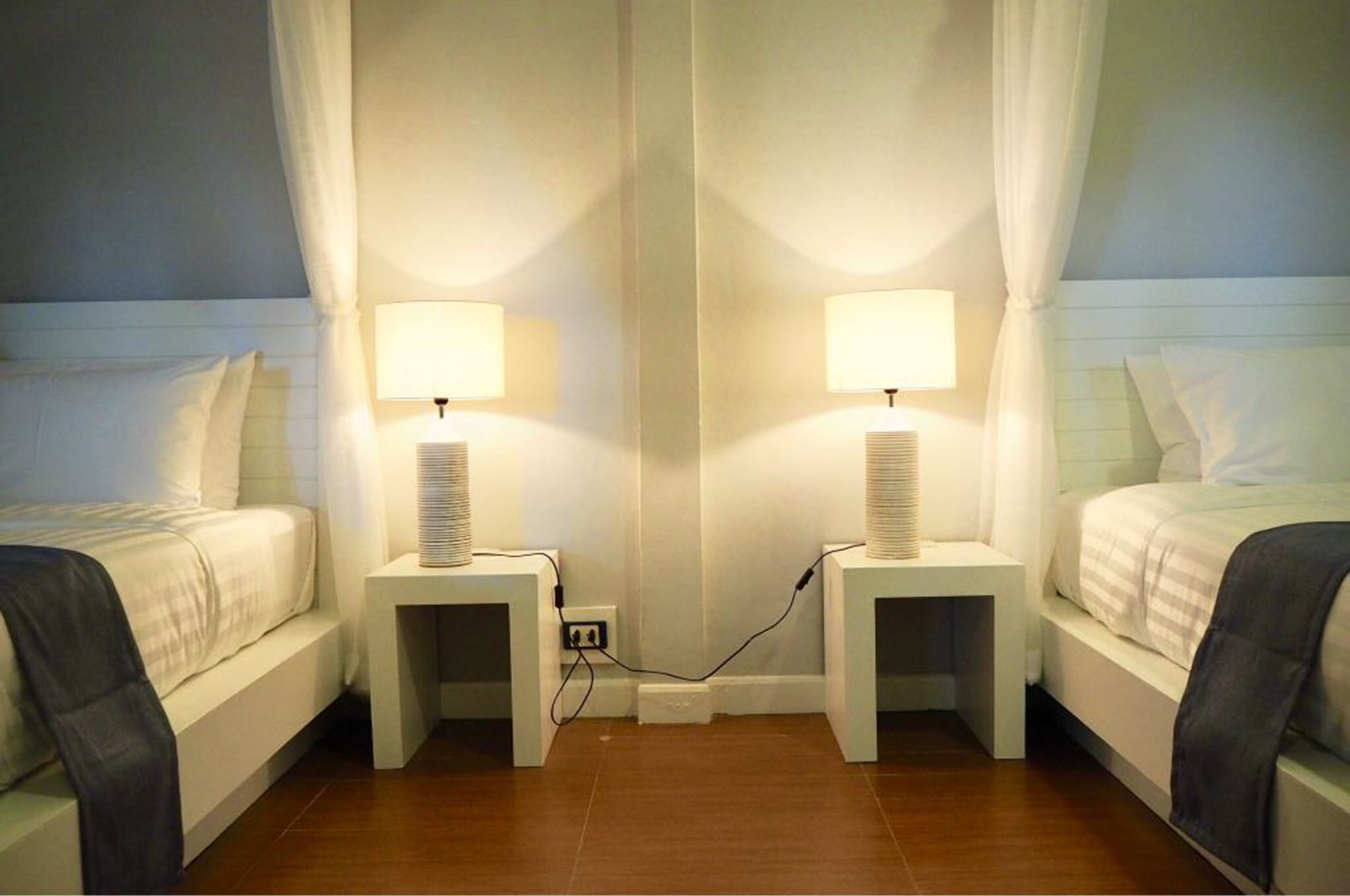 Ein Hotelzimmer mit zwei Betten, jeweils mit Nachttisch und Lampe, und einem großen Spiegel dazwischen.