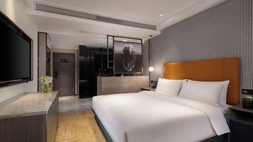 Una habitación de hotel moderna con una cama grande, un televisor de pantalla plana, un minibar y un baño con puerta de vidrio.