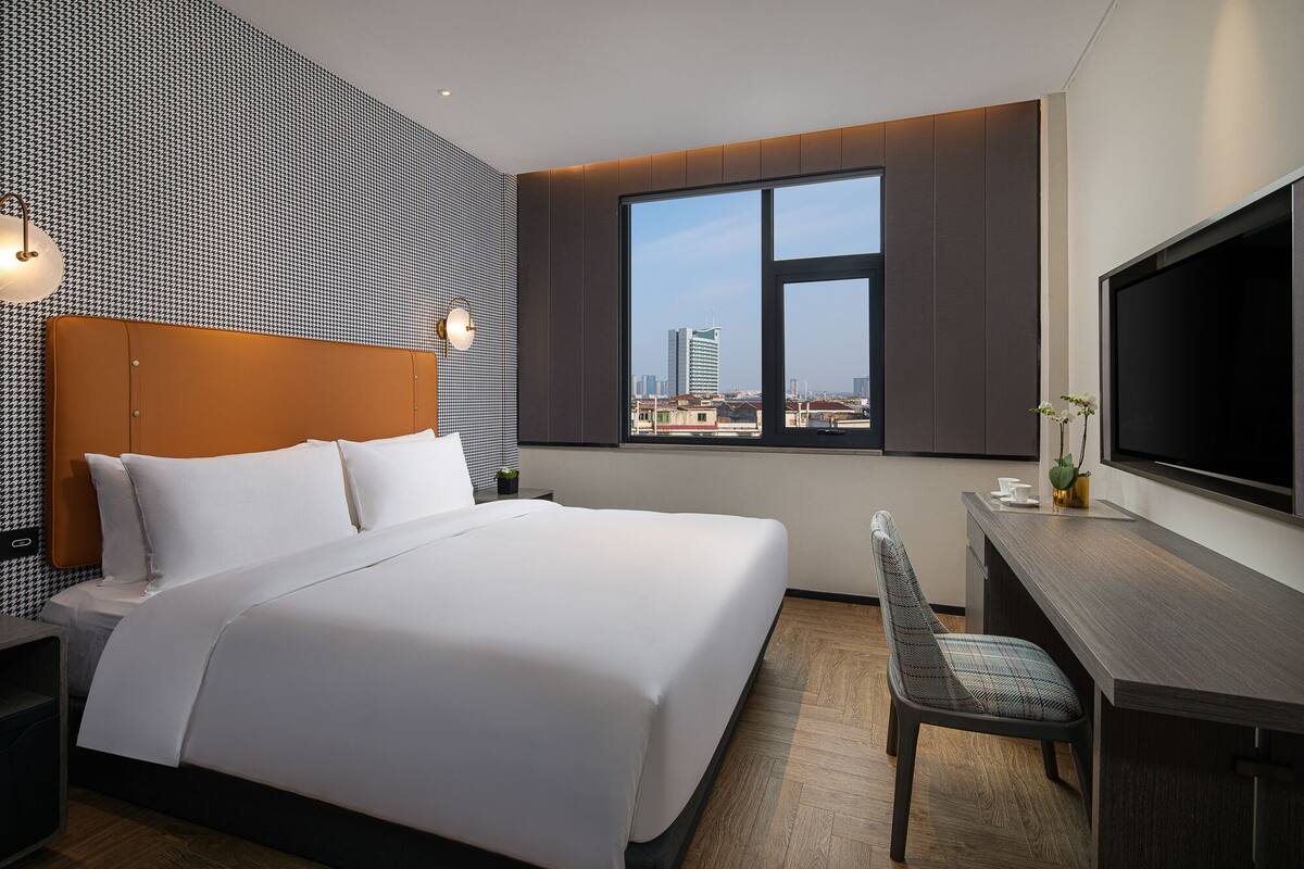 Habitación de hotel con una cama grande, un escritorio con silla, televisión y ventana con vistas a la ciudad.