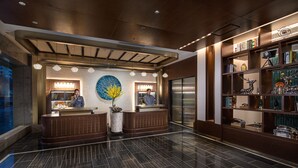 Um hall de hotel moderno com uma recepção, um grande painel decorativo e uma estante com diversos objetos.