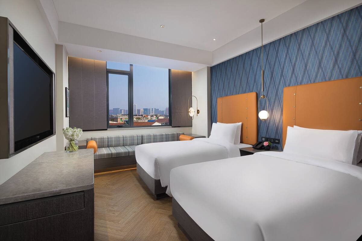 Habitación de hotel con dos camas, un sofá, un escritorio y un ventanal con vistas a la ciudad.