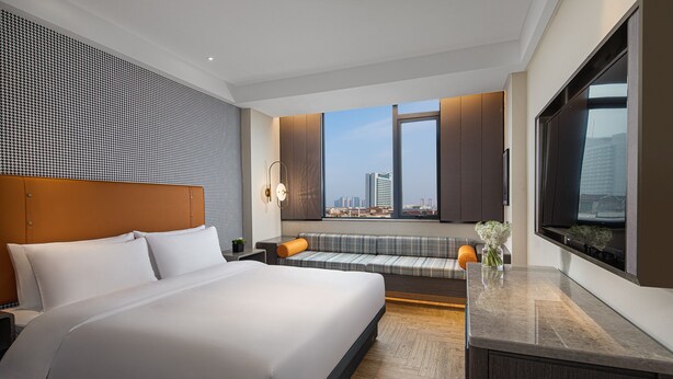 Quarto de hotel moderno com uma cama grande, um sofá, uma televisão e vista para a cidade.