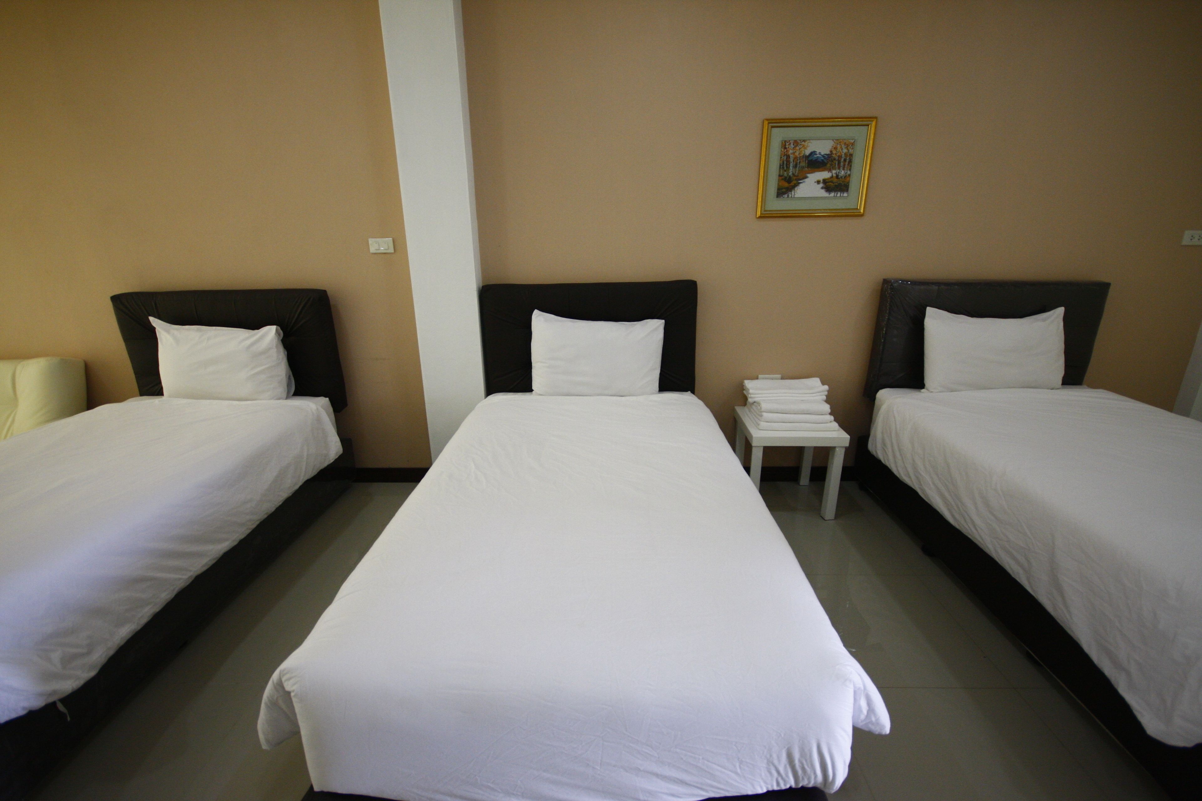 A hotel room with two single beds, a small table with a stack of white towels, and a framed picture on the wall.