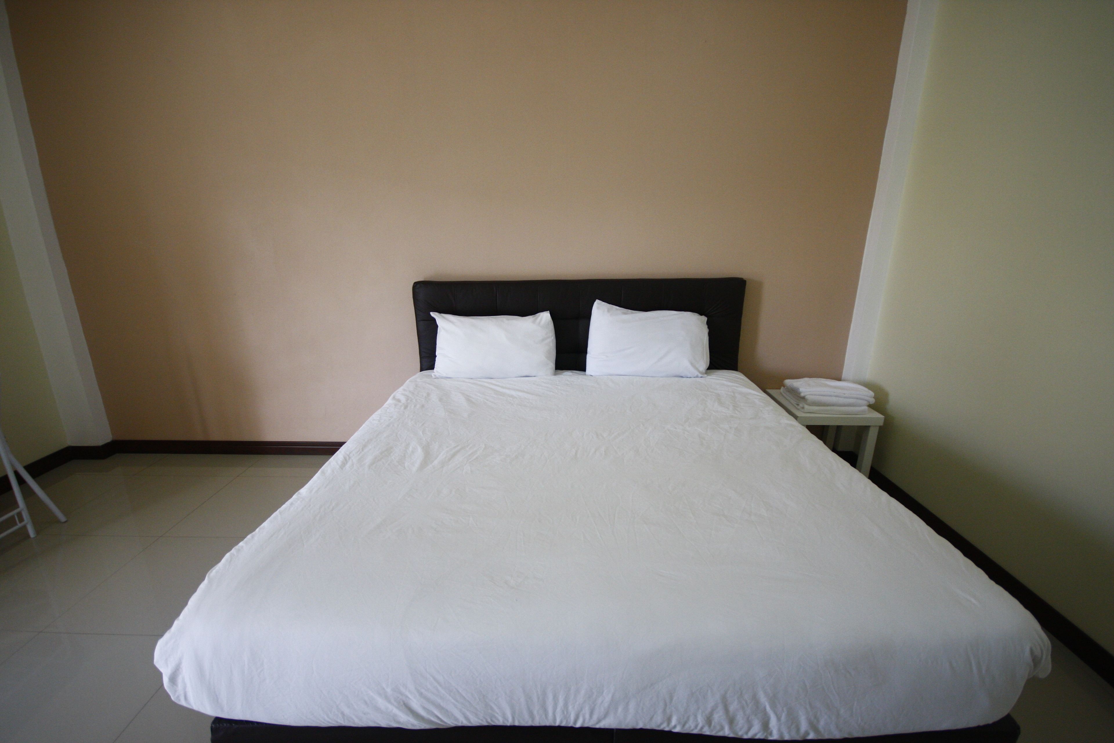 A neatly made bed with white linens in a room with beige walls and a small bedside table with a folded white towel.