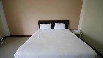 A neatly made bed with white linens in a room with beige walls and a small bedside table with a folded white towel.