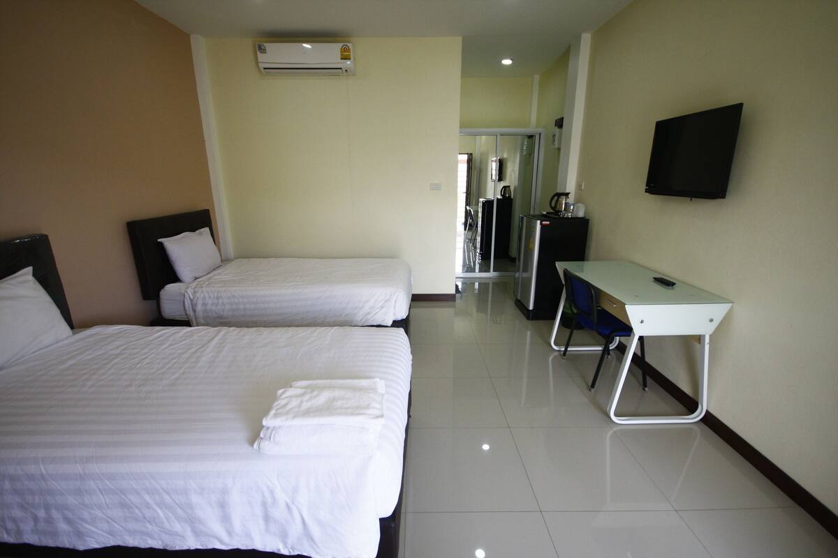 A hotel room with two beds, a desk, a chair, a TV, and an air conditioning unit.