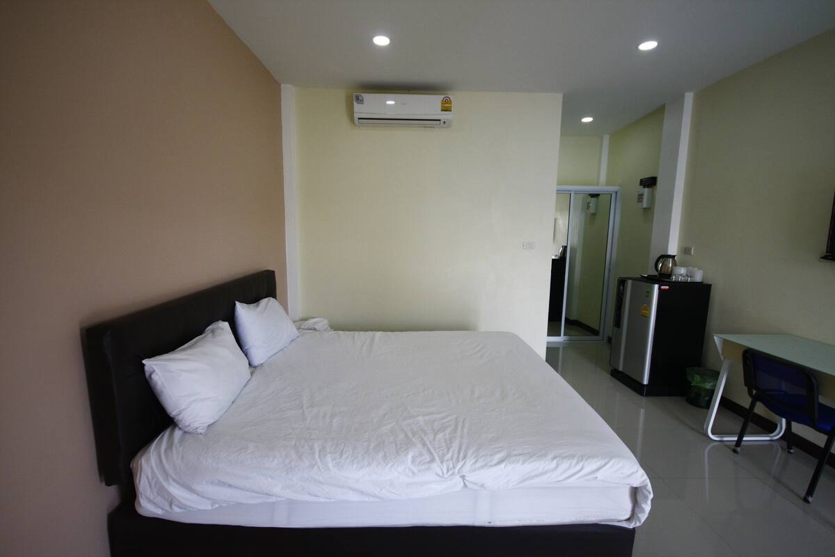 A hotel room with a bed, a desk, a mirror, and an air conditioning unit.