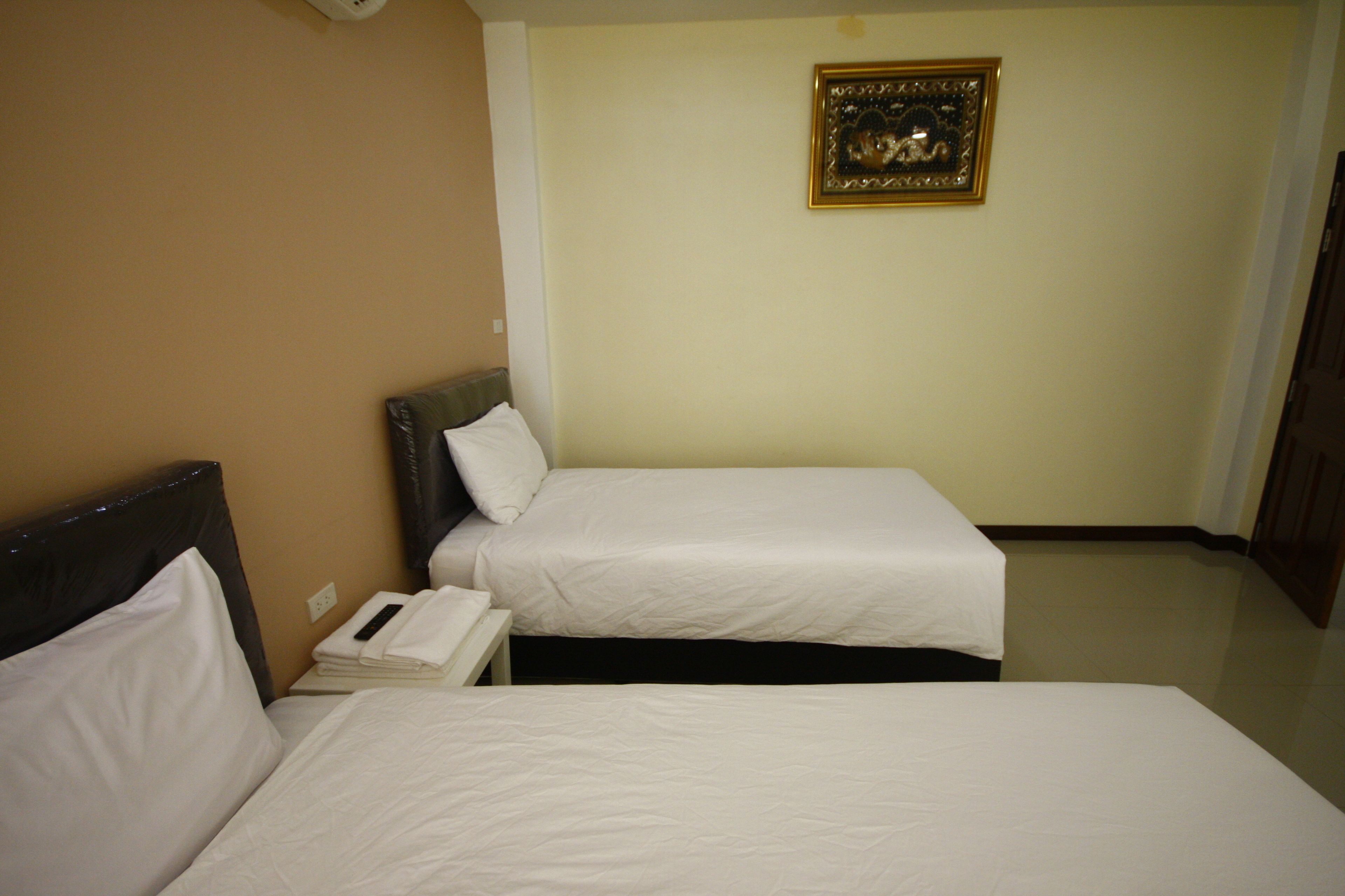 Ein Hotelzimmer mit zwei Einzelbetten, einem Nachttisch mit Fernbedienung und einem gerahmten Bild an der Wand.
