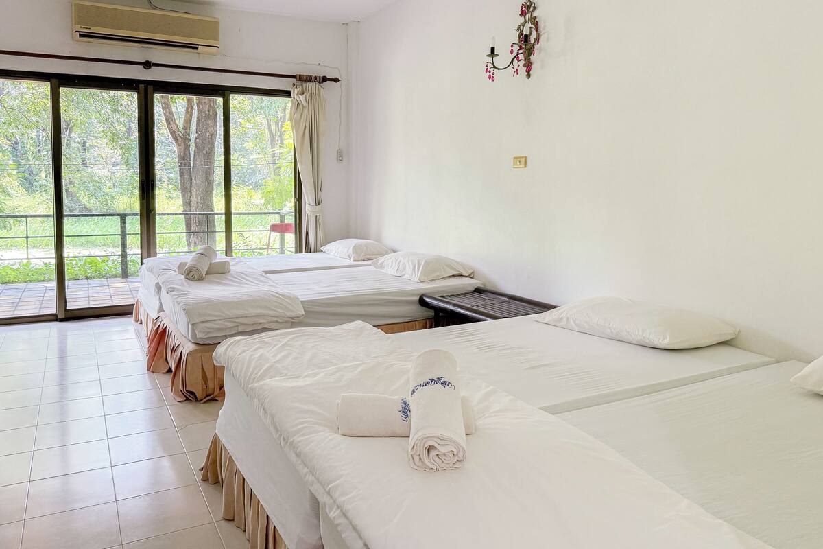 A hotel room with three beds, a sliding glass door to a balcony, and a wall-mounted air conditioning unit.