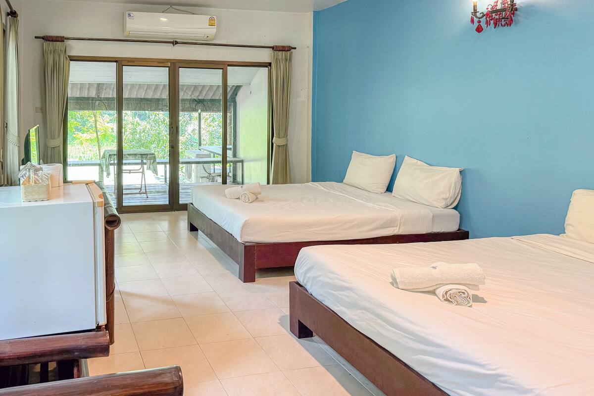 A hotel room with two beds, a desk, and a view of the outdoors.
