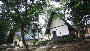 Un pequeño edificio blanco con techo inclinado, rodeado de árboles y un sendero de tierra.