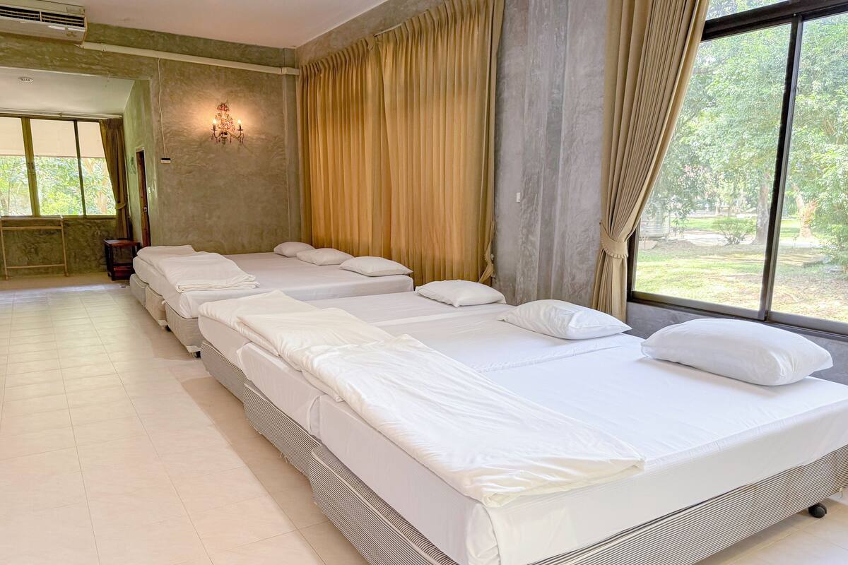 A hotel room with a long row of beds, a large window with curtains, and a wall-mounted light fixture.