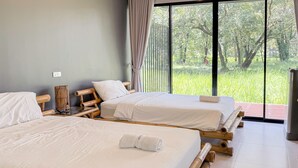 Habitación con dos camas, cada una con sábanas blancas y cabeceros de madera. Un amplio ventanal ofrece vistas al verdor exterior.