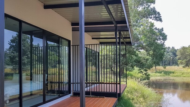 Un edificio moderno con amplios ventanales de vidrio, una terraza de madera y vistas a un estanque.
