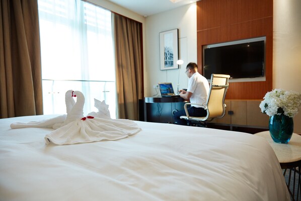 A hotel room with a bed, a desk with a laptop, a TV, and a vase with flowers. - The Thousand Lantern Lake Hotel (Foshan)
