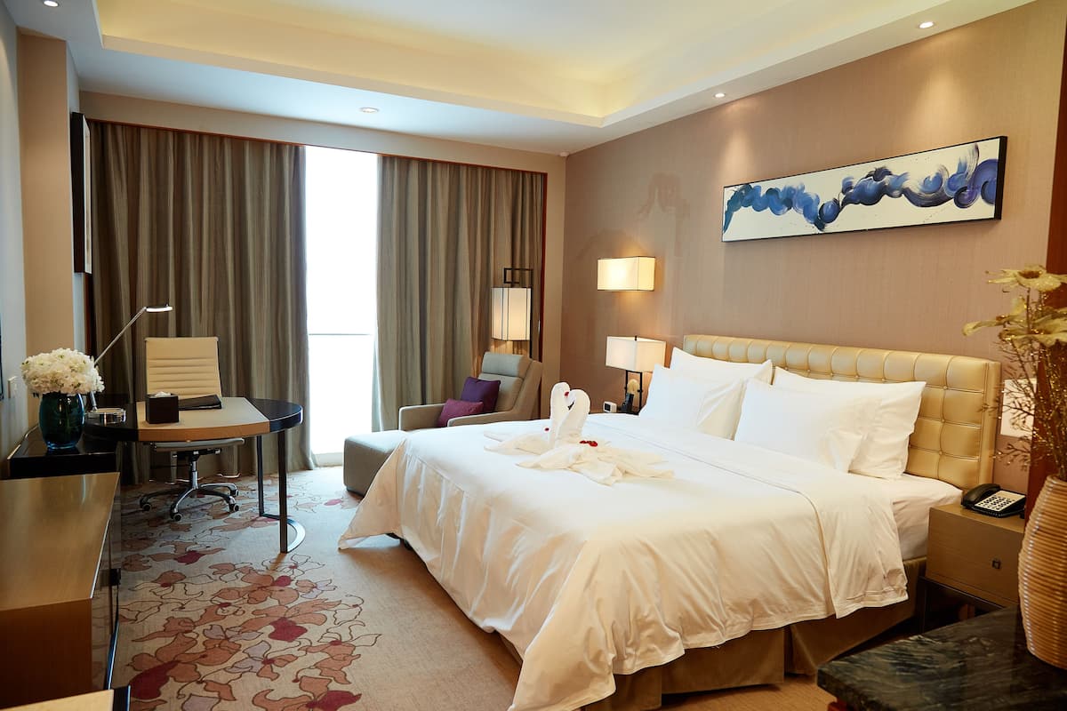 Une chambre d’hôtel avec un grand lit, un bureau avec une lampe, une chaise, un vase avec des fleurs et un tableau au mur.