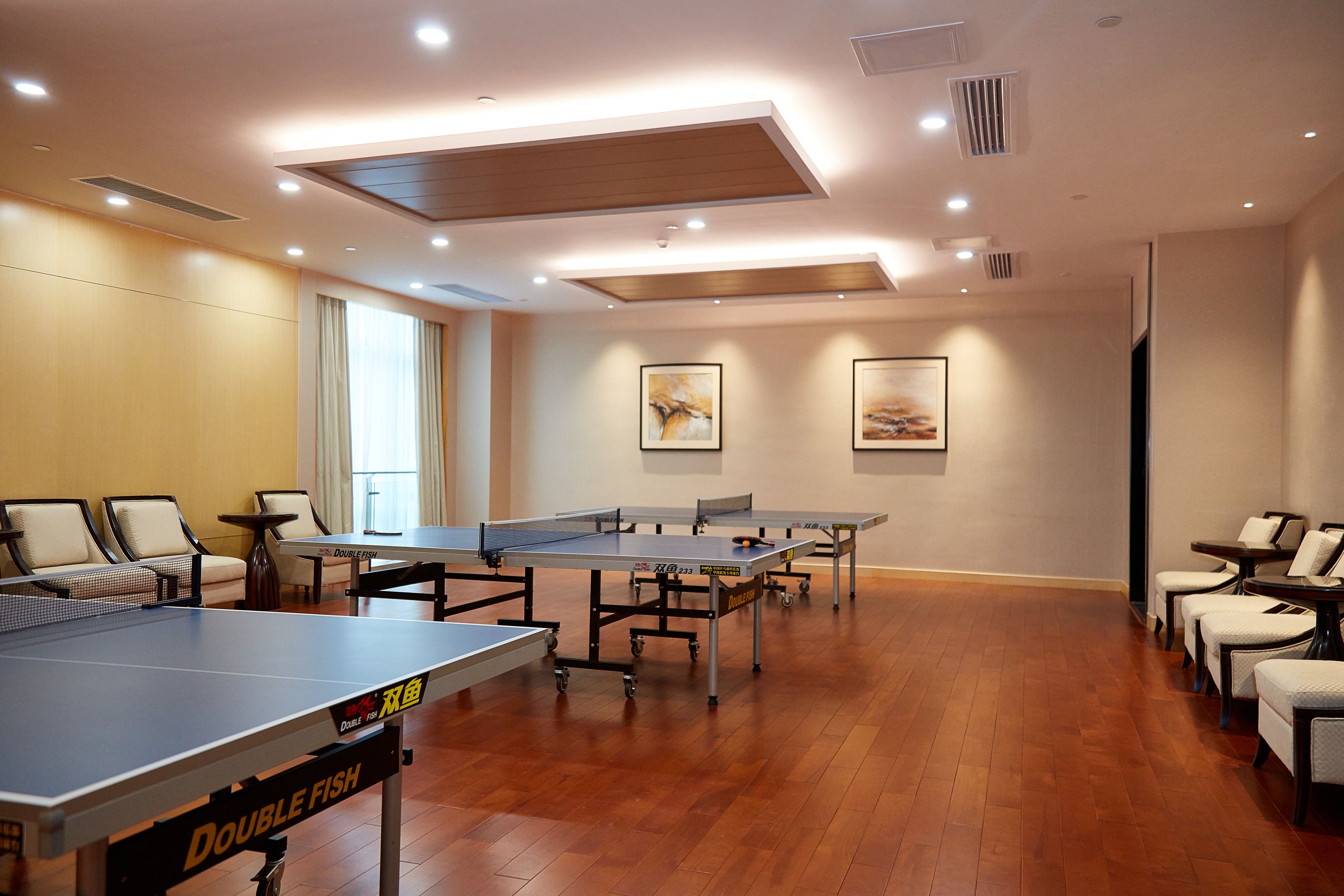 A spacious room with multiple ping pong tables, comfortable seating, and artwork on the walls.