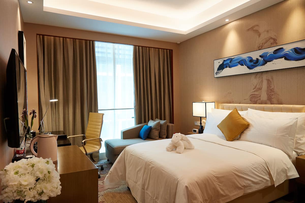 Une chambre d’hôtel avec un grand lit, un bureau, une chaise, une télévision et une fenêtre avec des rideaux.