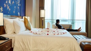 Une chambre d’hôtel avec un grand lit, un ordinateur portable posé sur le lit et une vue sur la ville par la fenêtre.