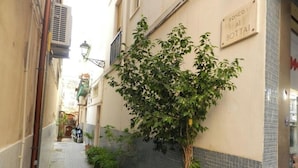 A narrow alleyway with a tree planted against a building wall, a tiled floor, and a sign with text. - Cavour Rooms (Syracuse)